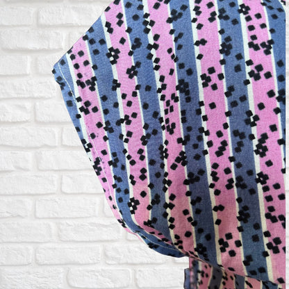 Fabric with pink, blue, and black pattern on a white brick wall background