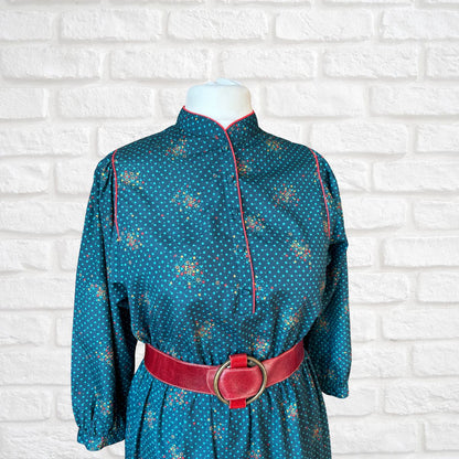 Blue patterned dress with a red belt on a mannequin against a white brick wall.