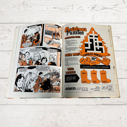 Open book with comic strip and Christmas puzzle on a wooden surface