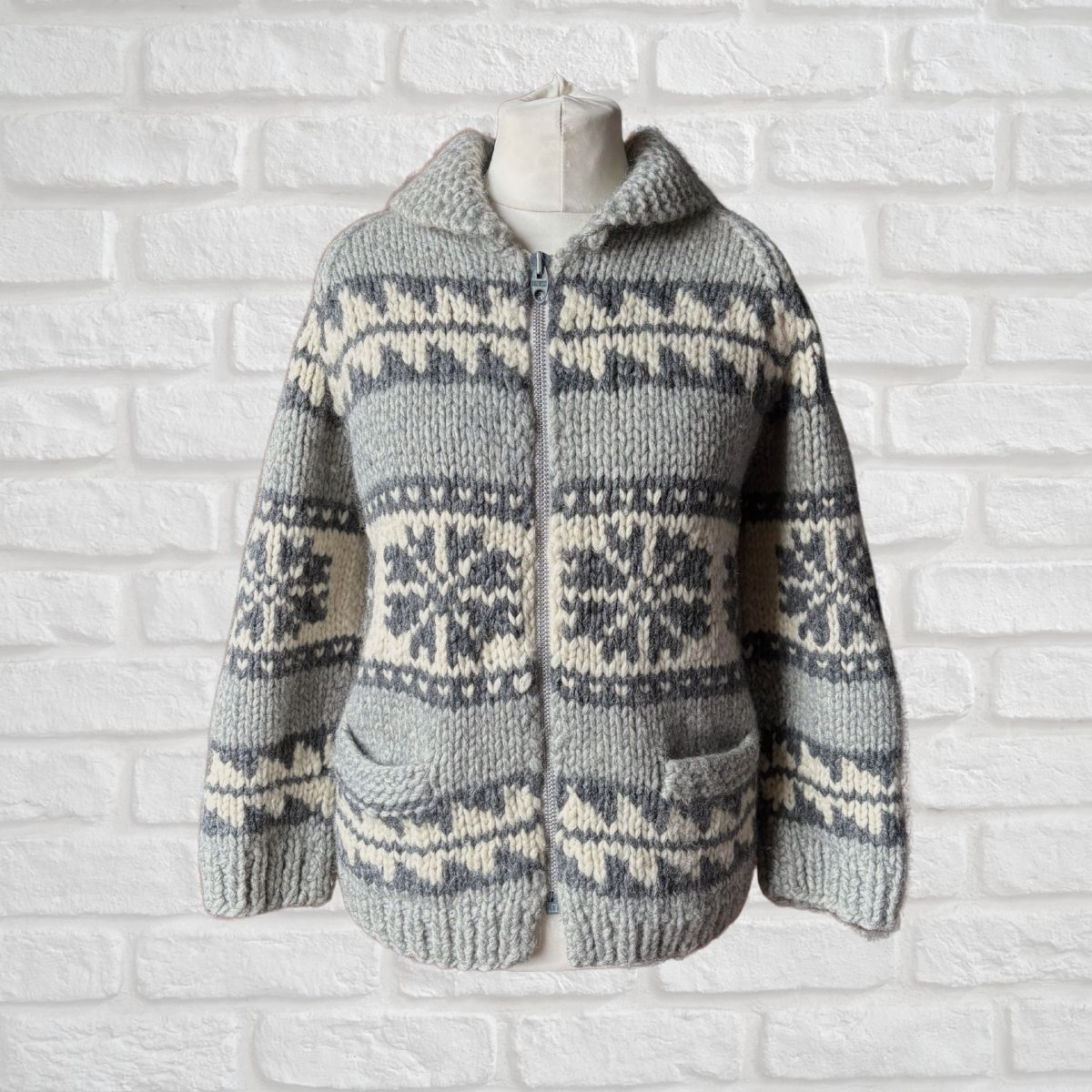 Knitted sweater with a snowflake pattern on a mannequin against a white brick wall.