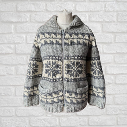 Knitted sweater with a snowflake pattern on a mannequin against a white brick wall.