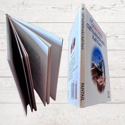 Book with open pages and a box labeled 'Cliff Babblebrook’s Raff Race' on a wooden surface