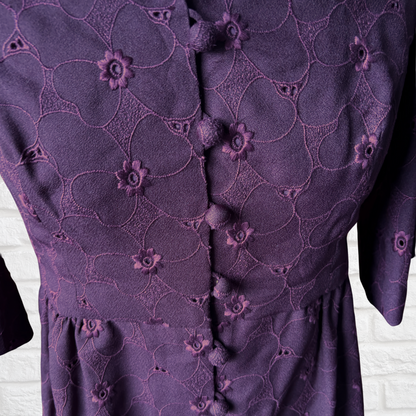 Close-up of a purple dress with floral embroidery on a white brick wall background