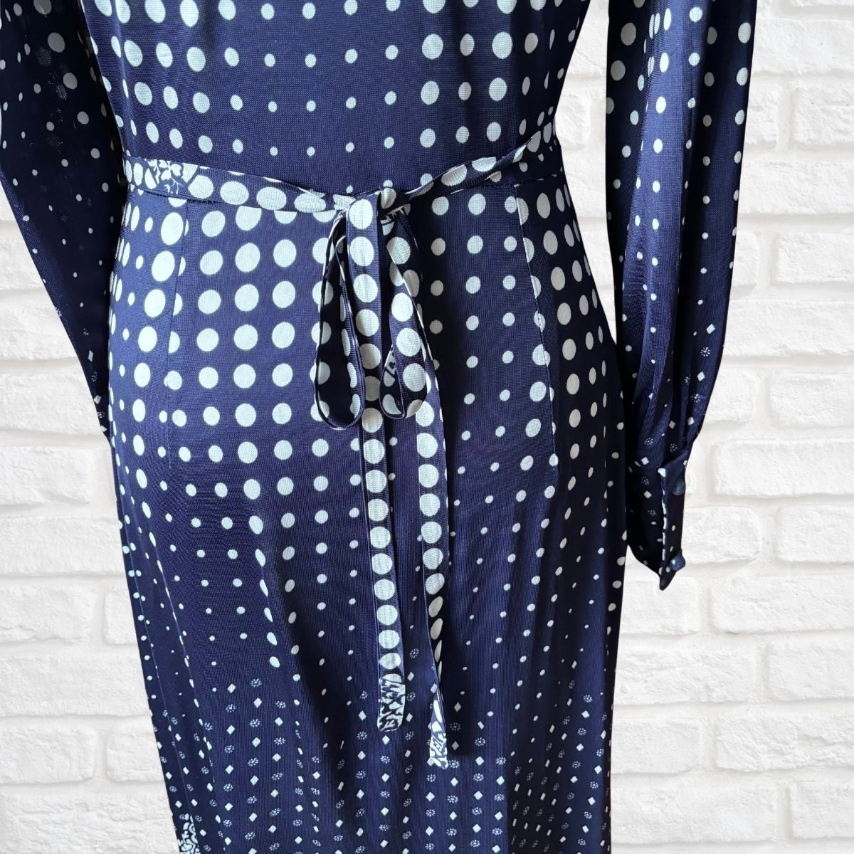 Navy blue dress with white polka dots against a white brick wall.