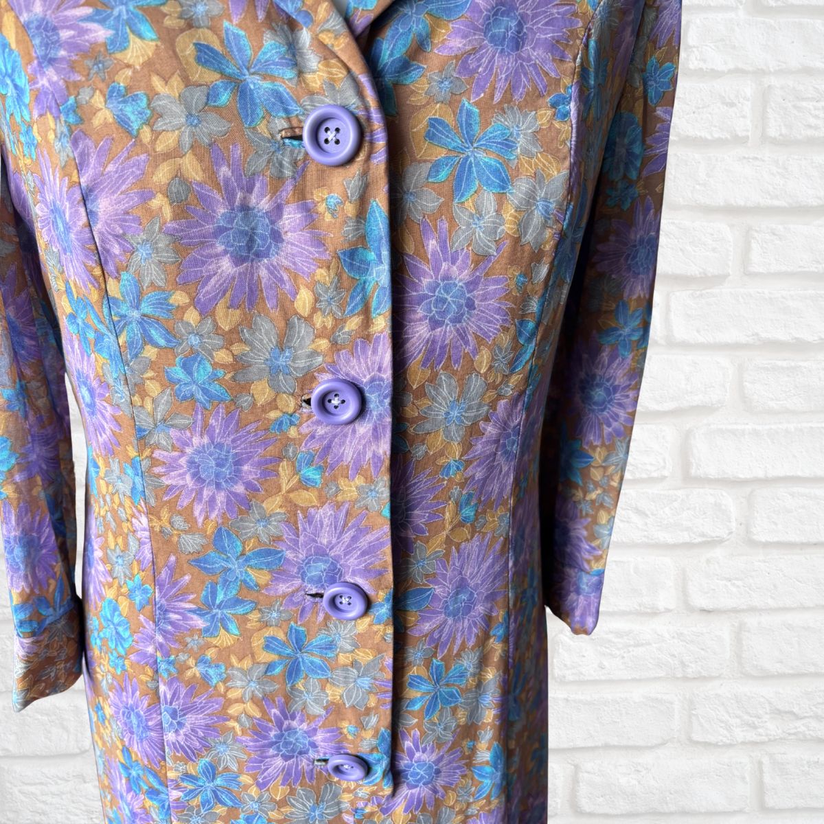 Floral patterned dress  with purple buttons on a white brick wall background