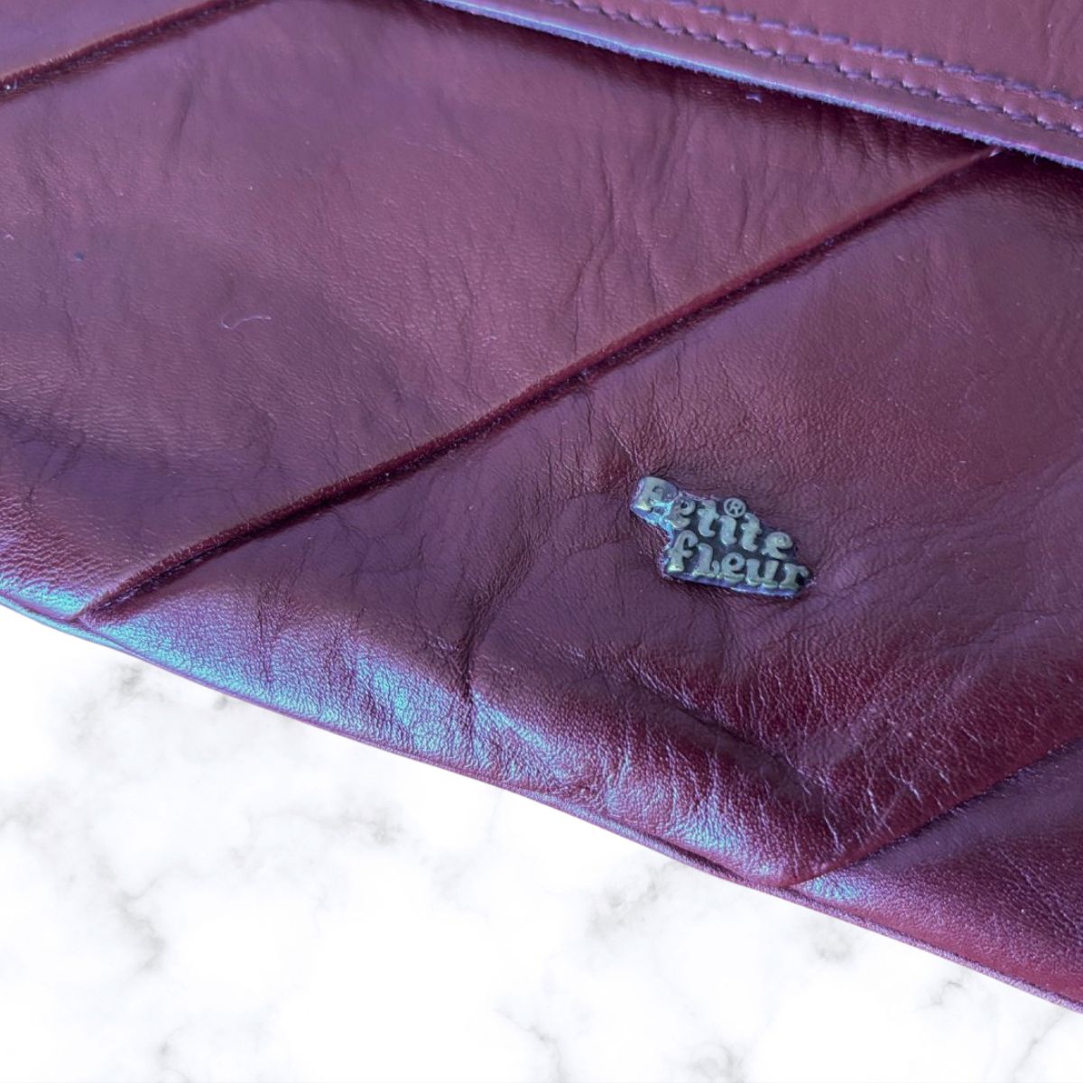 Close-up of a purple leather clutch with 'Petite Fleur' logo.