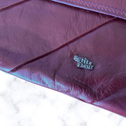 Close-up of a purple leather clutch with 'Petite Fleur' logo.