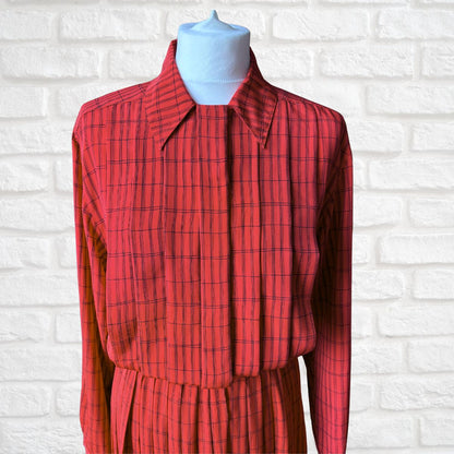 A red long-sleeve collared shirt dress with a thin black windowpane plaid pattern, displayed on a light blue mannequin torso against a white brick wall background.