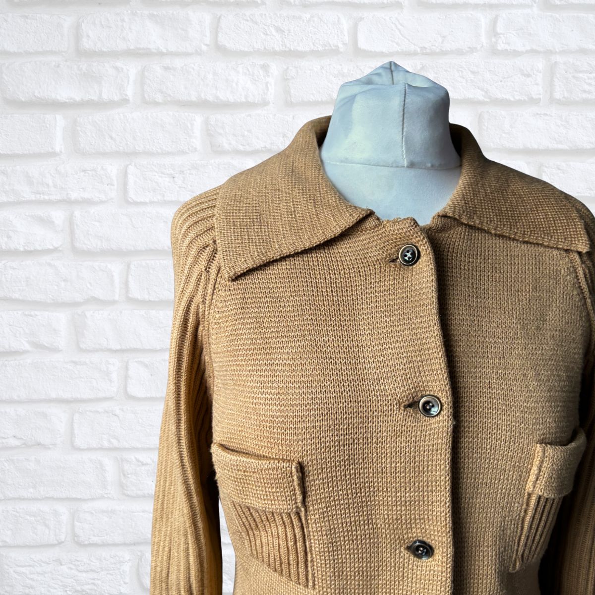 Camel knitted cardigan on a mannequin against a white brick wall.