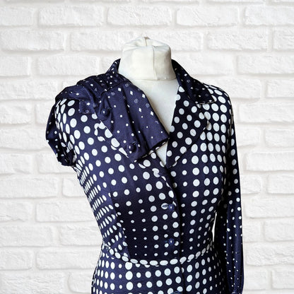 Navy blue shirt dress with white polka dots on a mannequin against a white brick wall.