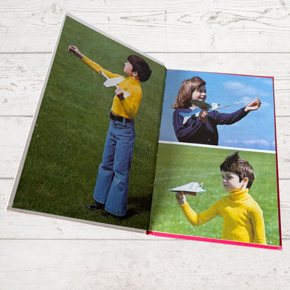 Open book showing three photos of a person with a kite on a grassy field.