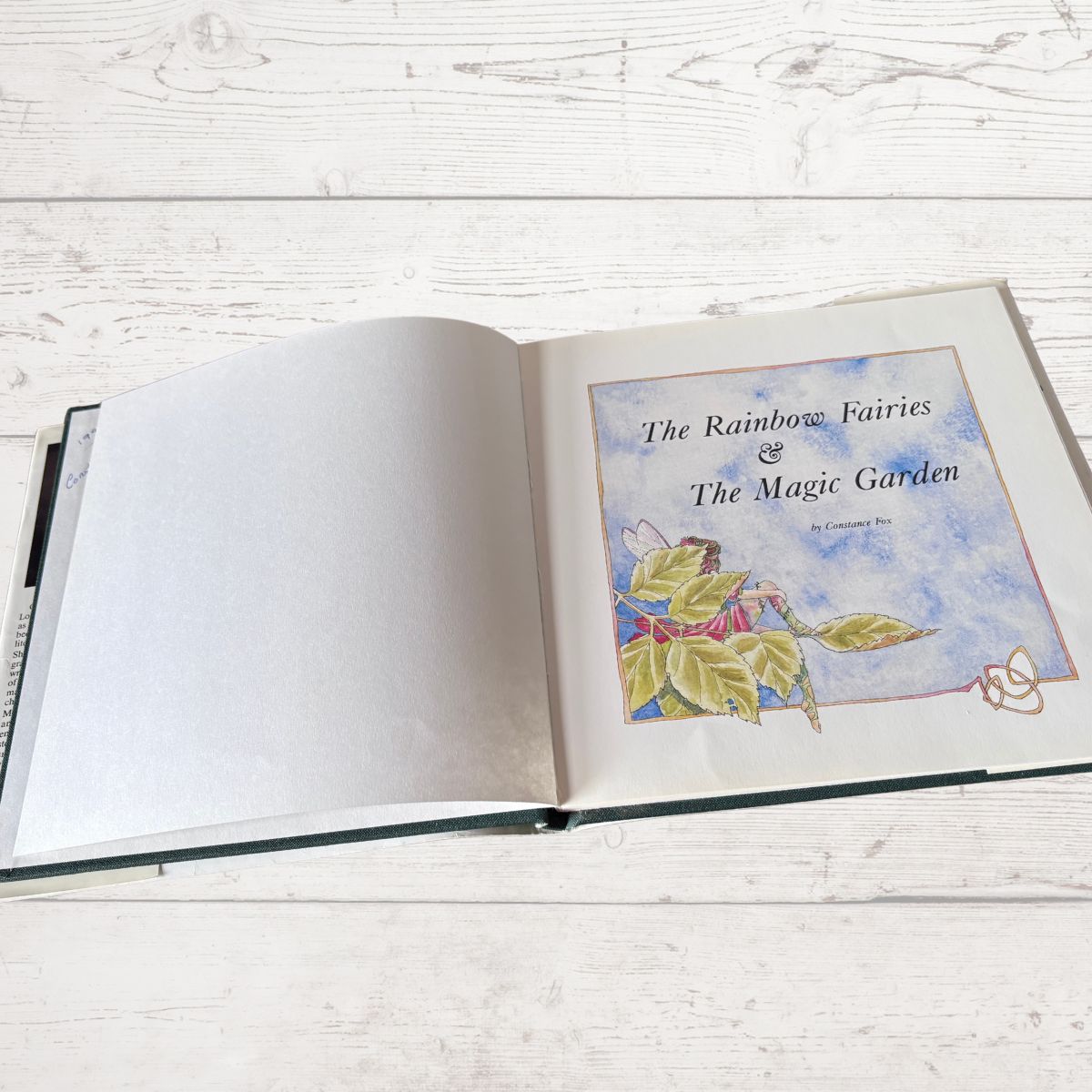 Open book titled 'The Rainbow Fairies & The Magic Garden' on a wooden surface