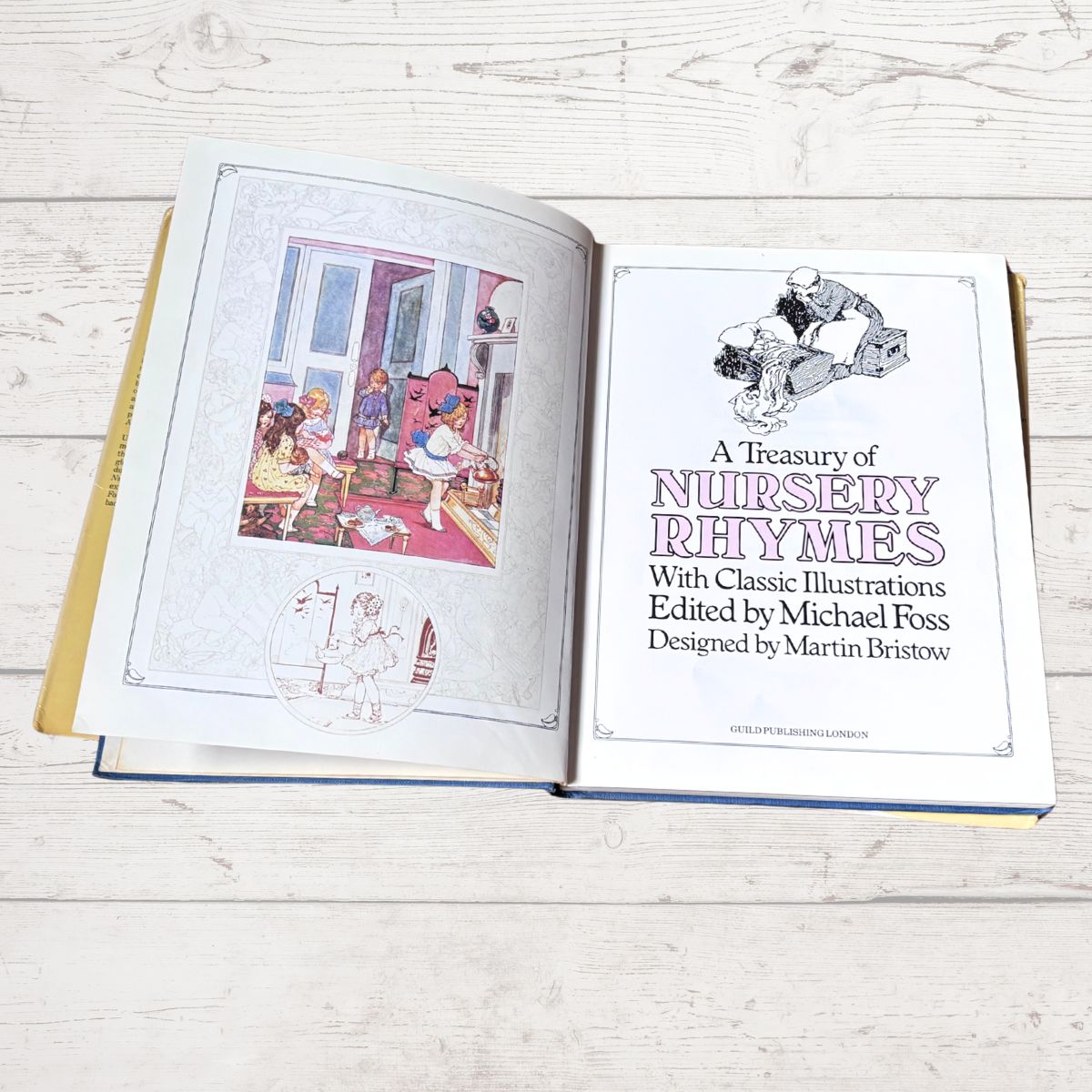 An open hardcover book titled 'A Treasury of Nursery Rhymes' lies on a light whitewashed wood surface. The left page shows a colorful nursery illustration, and the right page contains the title and author/editing credits in black text with pink lettering.