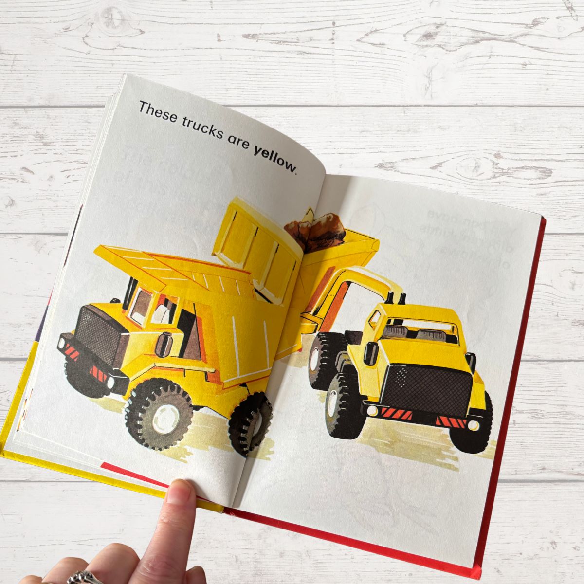 Open book showing illustrations of yellow trucks with text on a white wooden surface