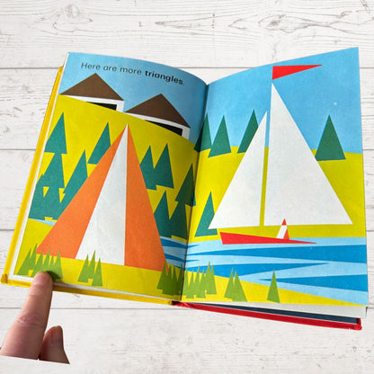 Open book showing colorful illustrations of sailboats and triangles on a wooden surface