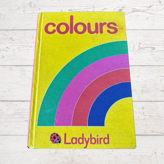 Book titled 'colours' by Ladybird with a rainbow design on a wooden surface