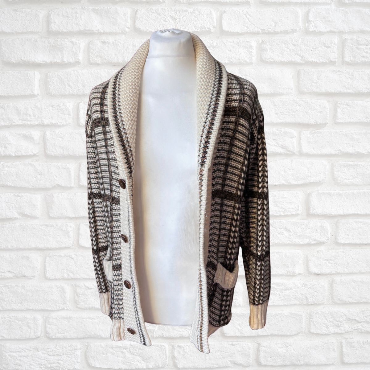 A brown and beige patterned knit cardigan sweater displayed on a white mannequin torso against a white brick wall background.