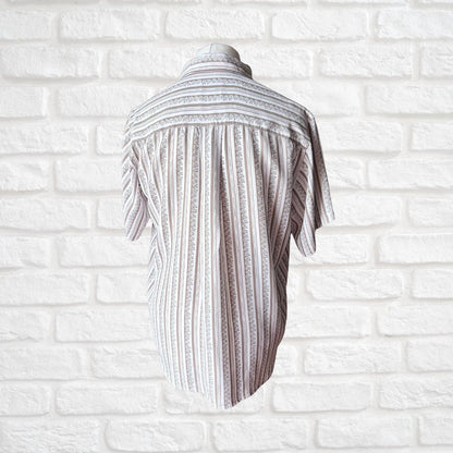 A short-sleeve button-up shirt with vertical textured stripes in white and gray, displayed on a mannequin torso against a white brick wall background.