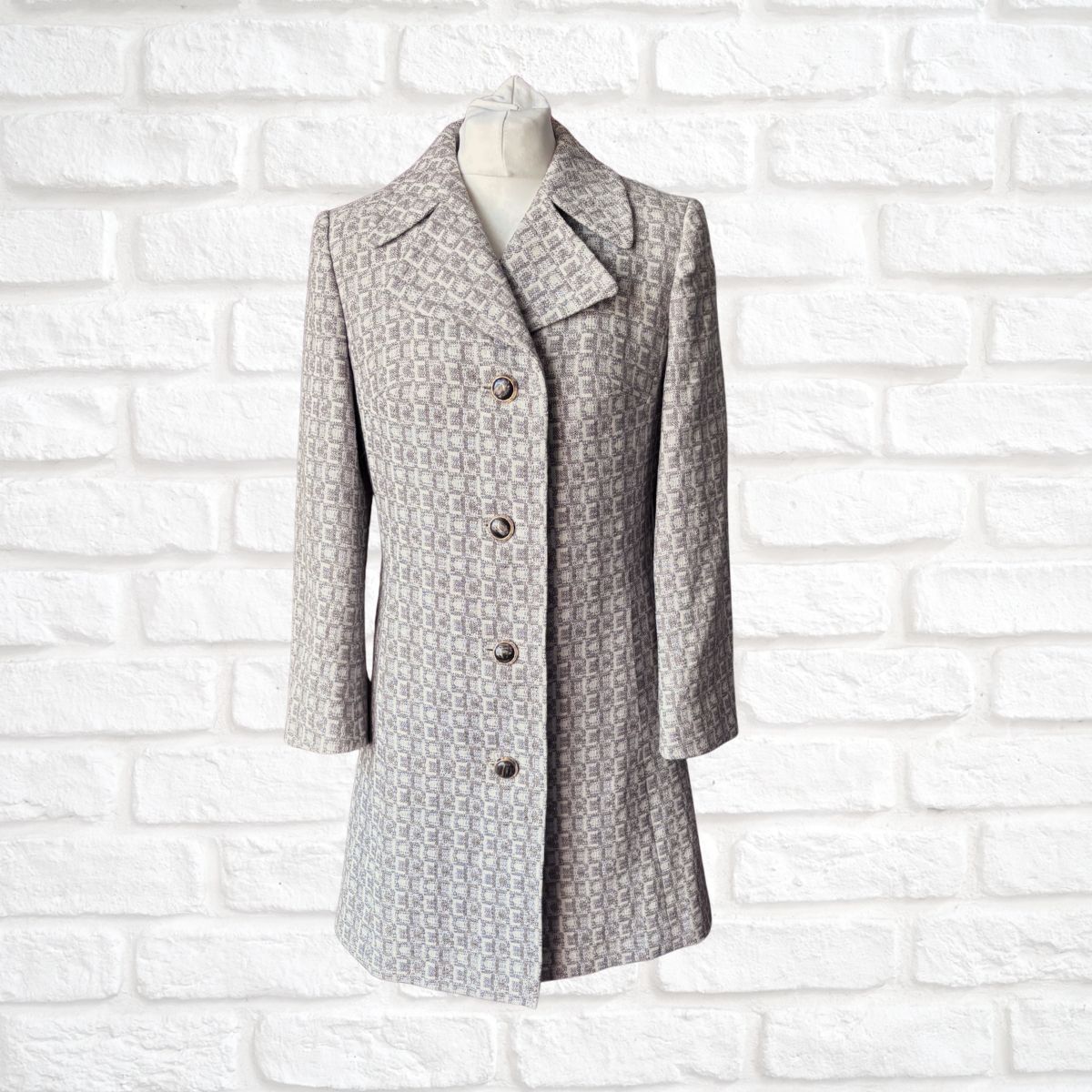 Grey tile patterned coat on a mannequin against a white brick wall background