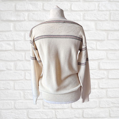 A cream-colored knit sweater with thin horizontal stripes displayed on a mannequin torso against a white brick wall background
