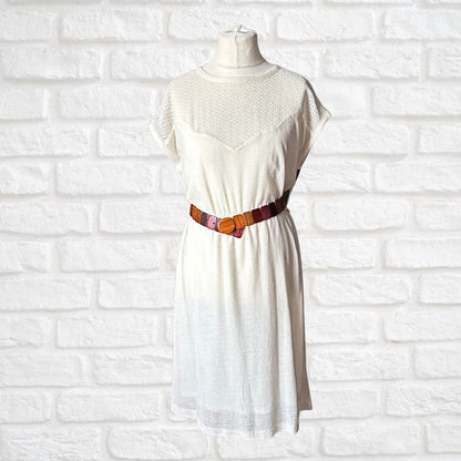 Cream dress with a brown  belt on a mannequin against a white brick wall.
