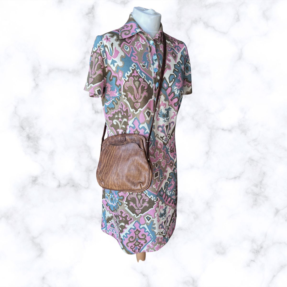 Mannequin wearing a patterned dress with a brown bag on a textured white background