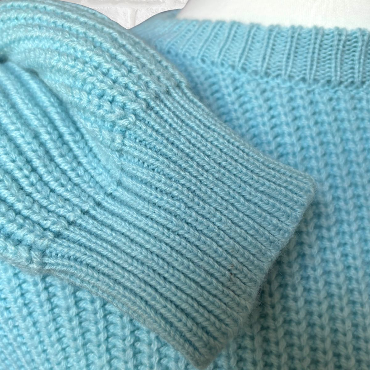 Close-up of a light blue ribbed knit garment, showing the texture of the sleeve cuff and matching knit body.