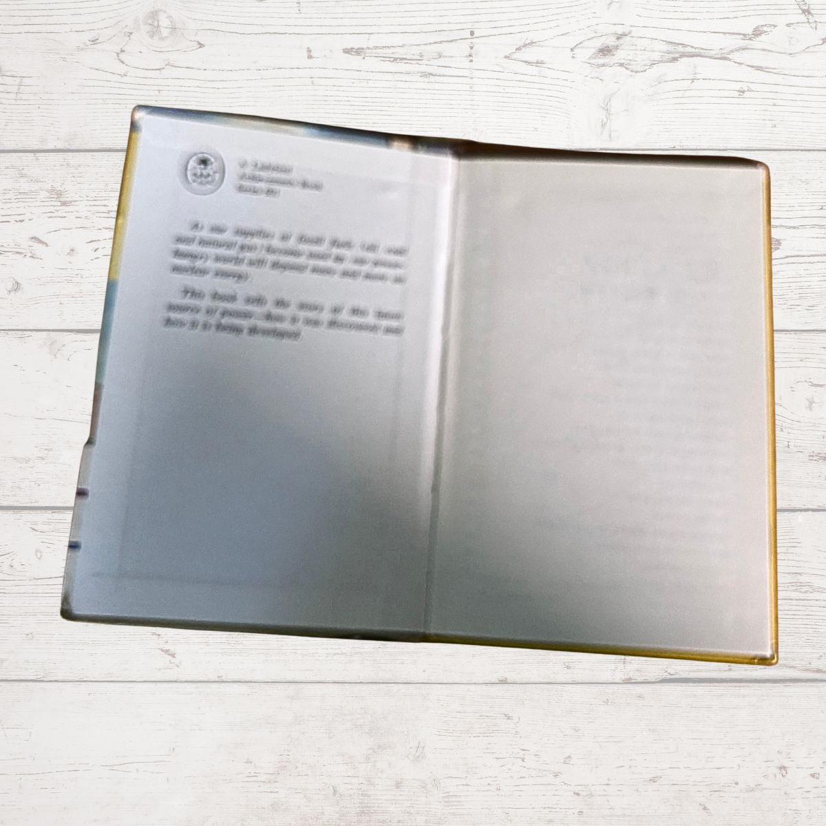 An open book  with printed text on the left page and a blank right page, placed on a light wood surface.