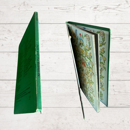 A hardcover book shown from multiple angles on a white wood plank background. One view shows the green spine with vertical title text, and the other shows the open floral-patterned interior pages.