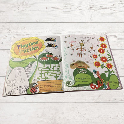 An open children's  book spread out on a white wood background, featuring colorful spring-themed illustrations, a flower maze, a flower pollinator puzzle, and a flower identification worksheet.