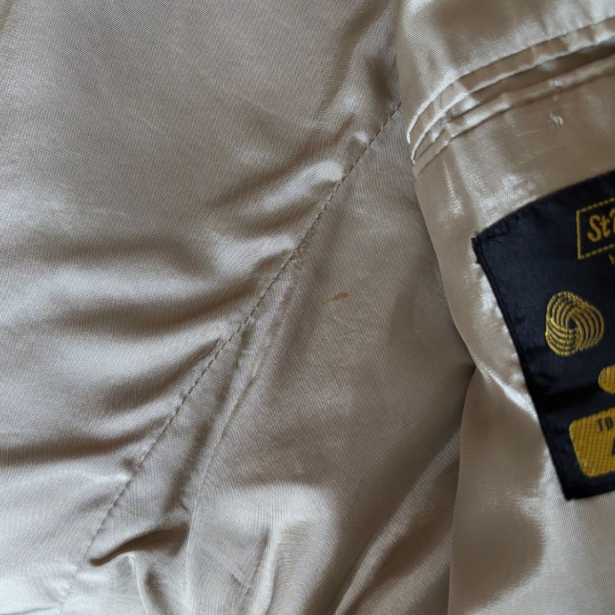 Close-up of a beige satin garment interior with a dark navy patch label featuring gold embroidery.