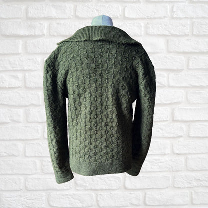 A dark green textured knit sweater displayed on a mannequin torso against a white brick wall background.