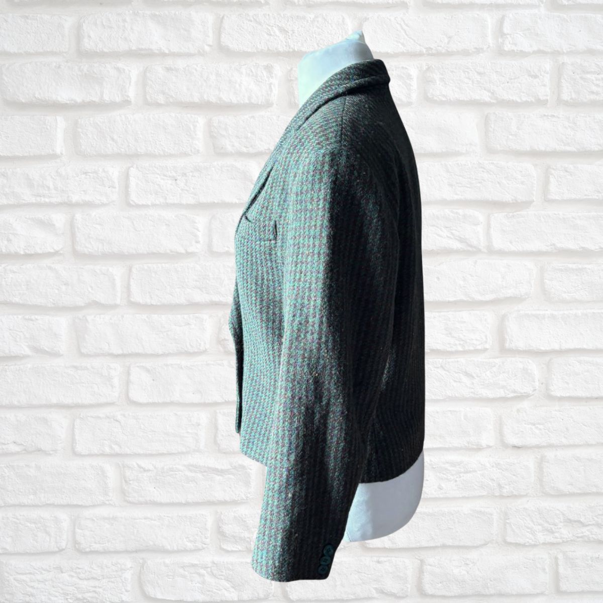 A dark green and brown textured knit cardigan sweater displayed on a mannequin torso against a white brick wall background.