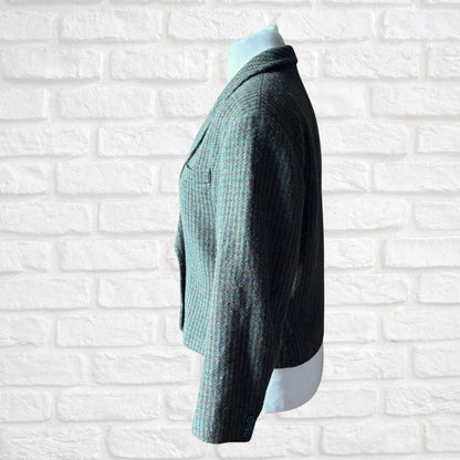 A dark green and brown textured knit cardigan sweater displayed on a mannequin torso against a white brick wall background.