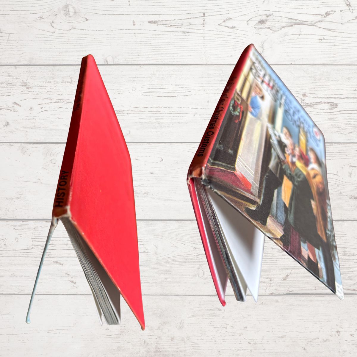 vintage hardcover book displayed as bookends on a light gray wood plank background. The left book is closed, showing a solid red cover with gold lettering that reads 'HISTOR.