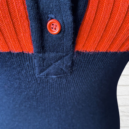 Close-up of a ribbed knit top or sweater with a color-block design, featuring a dark navy blue lower section, a bright orange-red yoke, and a matching orange-red button.