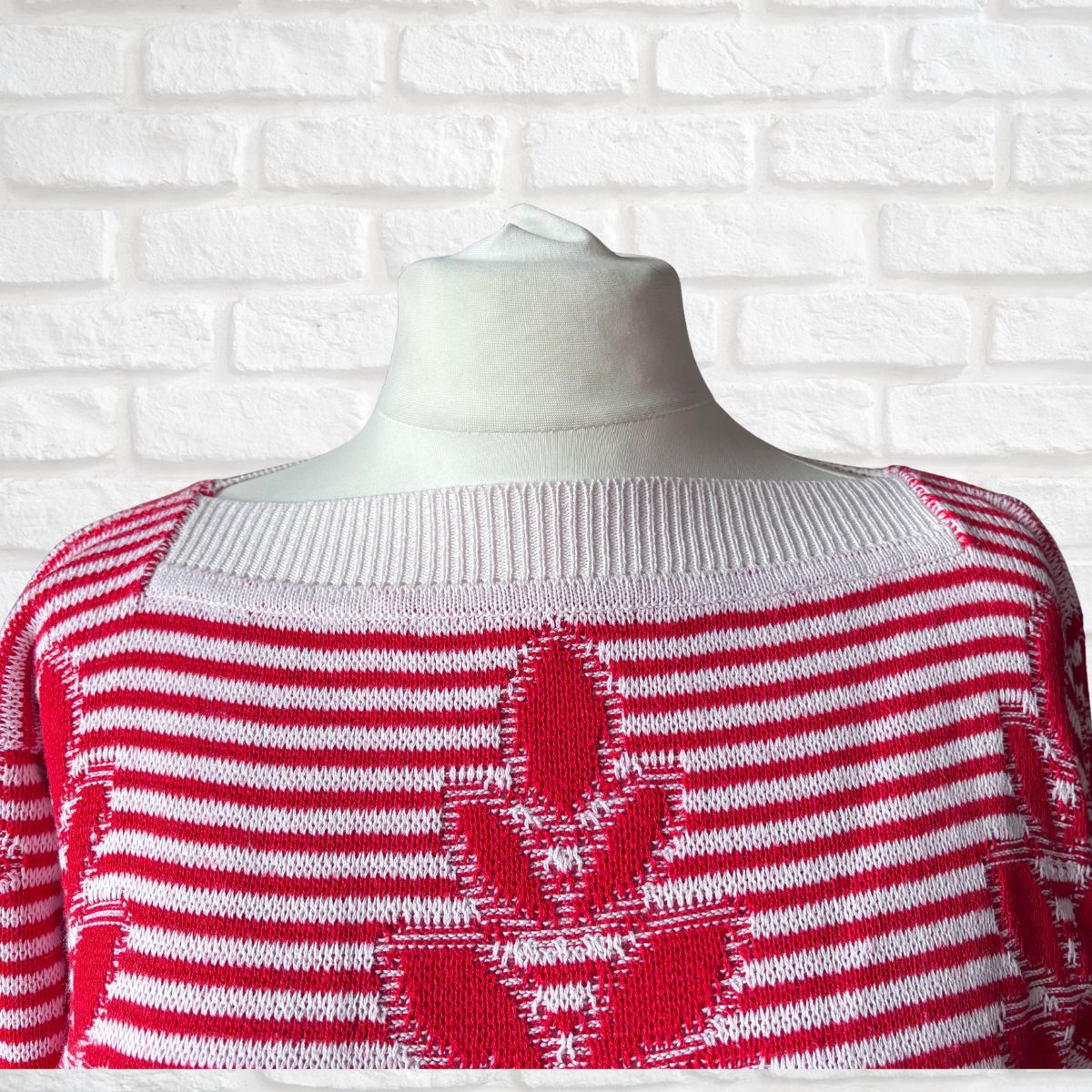 A red and white striped knit sweater displayed on a white mannequin torso against a white brick wall background.