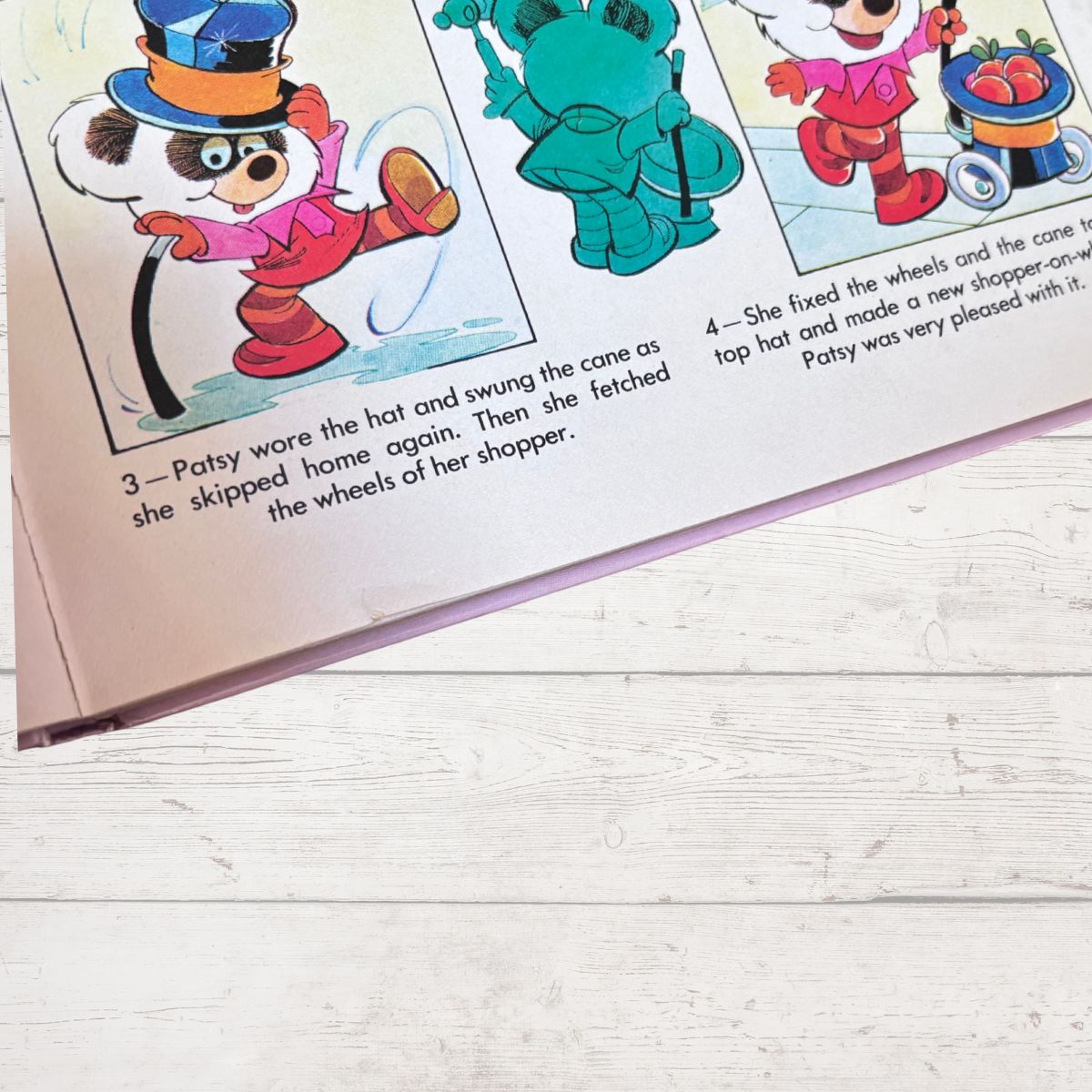 A close-up of a children's book page showing colorful cartoon animal illustrations and printed text, photographed on a light wood surface.