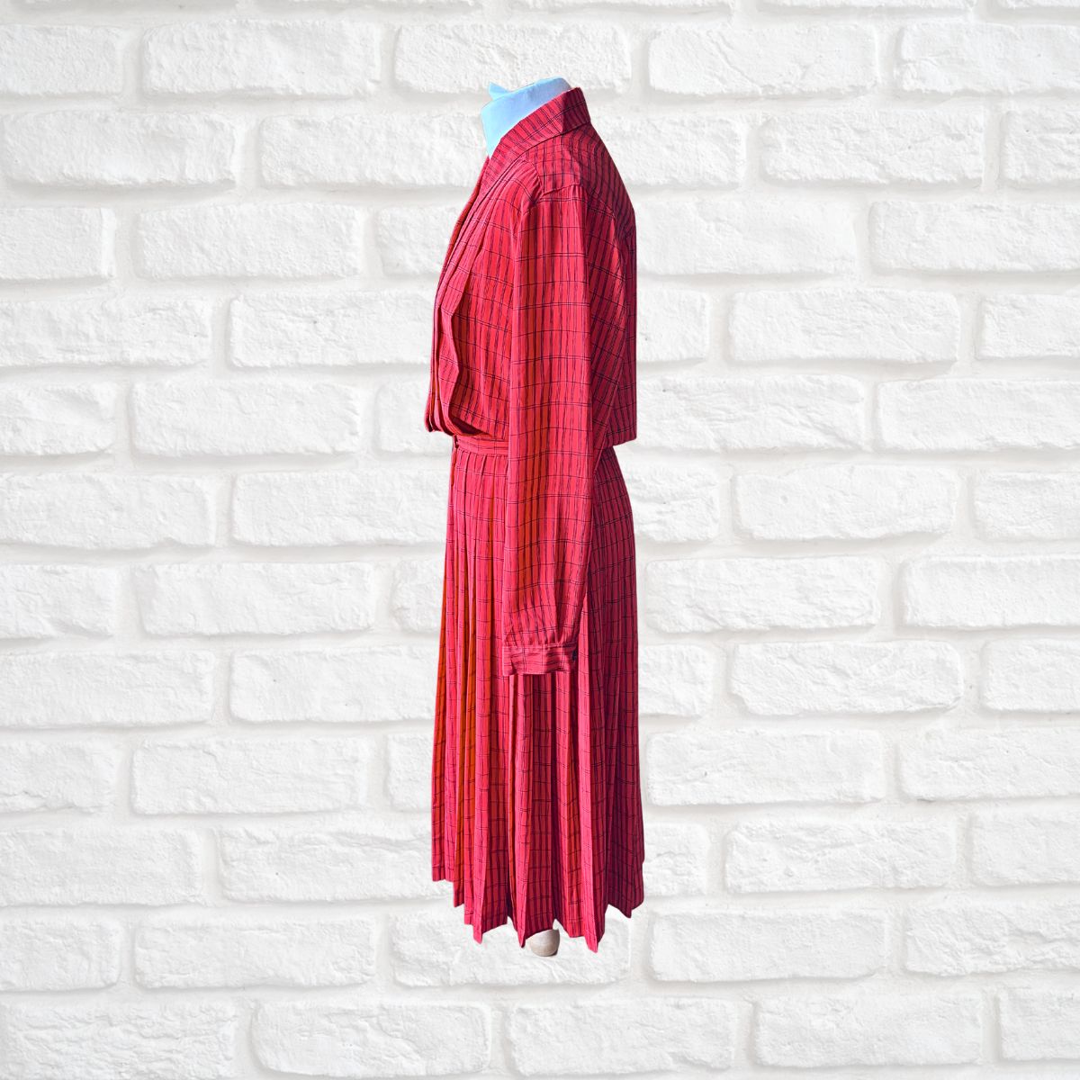 A red and black plaid long-sleeve dress displayed on a headless mannequin torso against a white brick wall background.