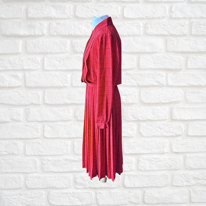 A red and black plaid long-sleeve dress displayed on a headless mannequin torso against a white brick wall background.