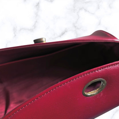 Close-up of a red  leather bag showing the interior lining, metal snap closure, and brass grommet detail against a white marble background.