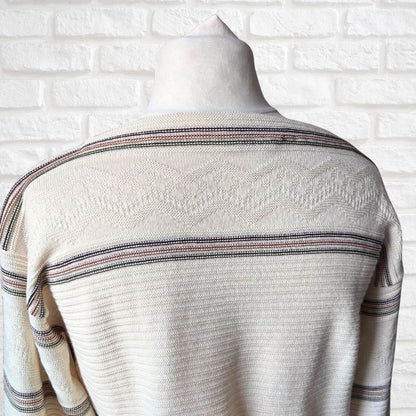 A cream-colored knit sweater with horizontal stripes  on a mannequin torso against a white brick wall background.