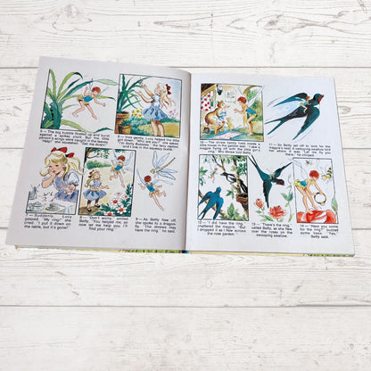 An open children's picture book spread on a whitewashed wooden surface, showing illustrated fairy tales with multiple panels and small text blocks.