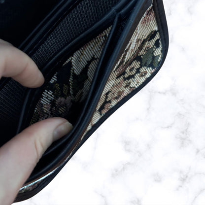 A close-up of a black bag being opened by a hand, showing patterned interior card slots on a white marble surface.