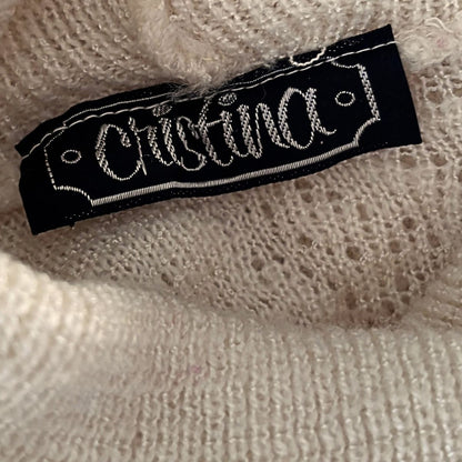 Close-up of a cream-colored knit sweater with a black fabric brand label reading 'Cristina' in white script.