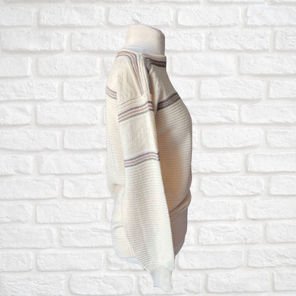 A cream-colored knit sweater with thin horizontal stripes in green and brown, displayed on a mannequin torso against a white brick wall background.
