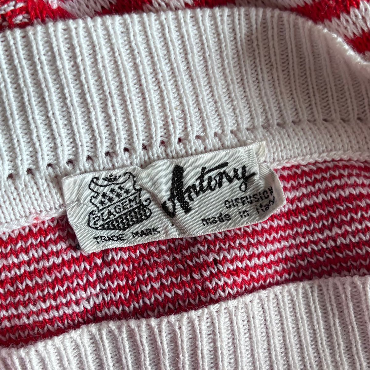 Close-up of a knit garment label reading 'Anthony' and 'Diffusion made in Italy' on a white ribbed knit fabric with red and white striped knit bands.
