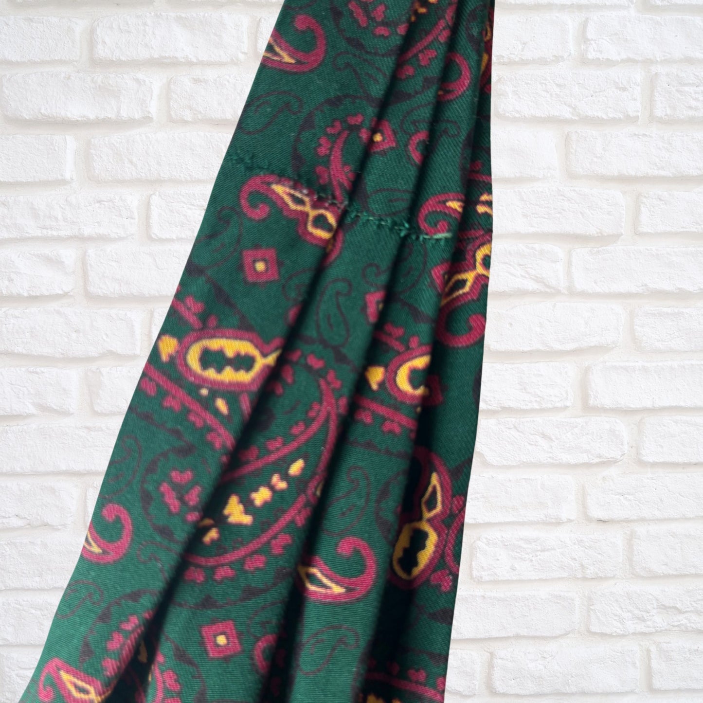 Green cravat with red and yellow pattern on a white brick wall background