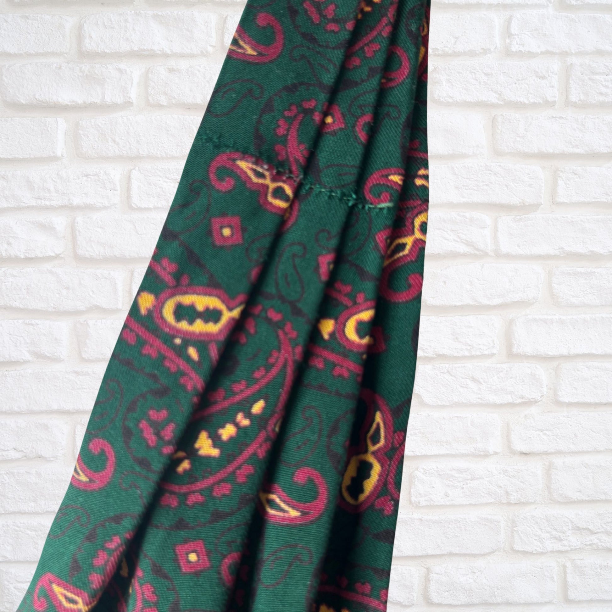 Green cravat with red and yellow pattern on a white brick wall background