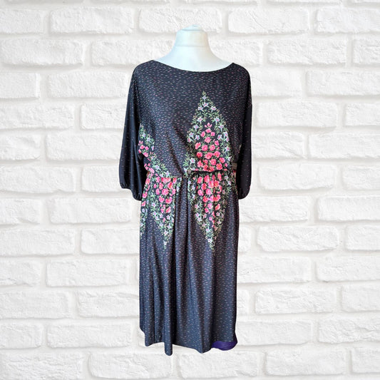 Black dress with floral patterns on a mannequin against a white brick wall.